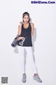 A woman in a black tank top and white leggings holding a yoga mat.