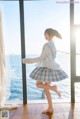 A young woman in a plaid skirt is dancing in front of a window.