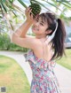 A woman in a floral dress holding a bunch of pineapples.