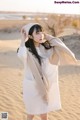 A woman in a white dress and hat standing in the sand.