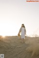 A woman in a white dress standing in the sand.