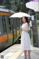 A woman in a white dress holding an umbrella at a train station.