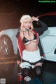 A woman in a maid outfit posing in front of a car.