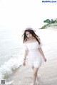 A woman in a white dress and hat walking on the beach.