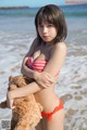 A woman in a bikini holding a teddy bear on the beach.