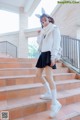 A woman in a white jacket and black skirt standing on some steps.