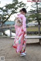 A woman in a pink kimono standing next to a pond.