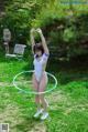 A woman in a white bathing suit playing with a hula hoop.