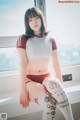 A woman sitting on a window sill with tattoos on her legs.