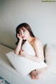 A woman sitting on a white couch with a pillow.