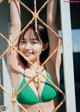 A woman in a green bikini posing behind a fence.