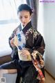 A woman in a black kimono sitting on a couch holding a fan.