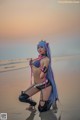 A woman with long blue hair is posing on the beach.
