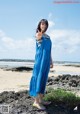 A woman in a blue dress standing on a beach.