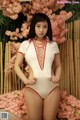 A woman in a white bodysuit posing in front of pink flowers.